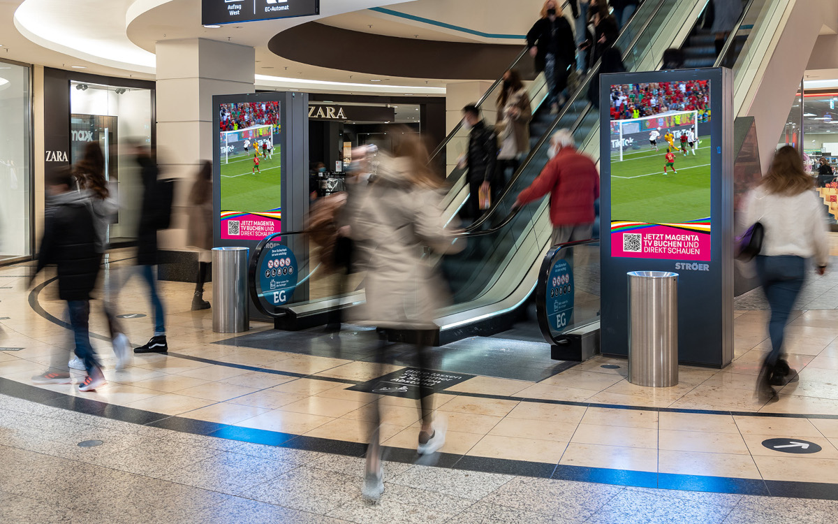 Die DooH-Torszenen werden unter anderem in Einkaufszentren zu sehen sein. (Fotomontage: Deutsche Telekom/Ströer)