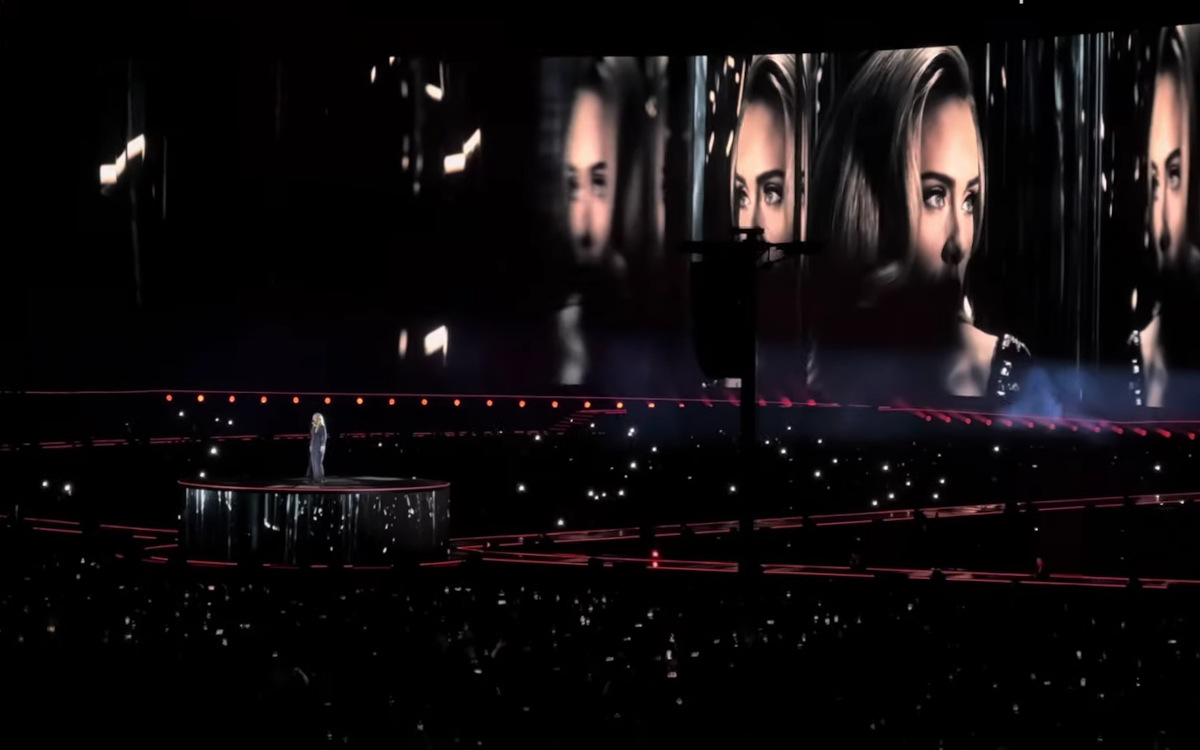 Während Adele auf einem Podium singt, läuft auf dem Megascreen im Hintergrund eine maßgeschneiderte Videoshow ab. (Foto: Screenshot/ In Concert)