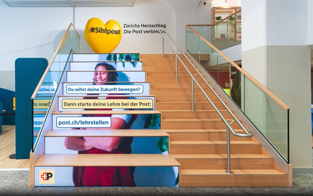 Auf den Stufenfronten der Sitztribüne spielt die Post eigene Inhalte aus. (Foto: Umdasch The Store Makers)